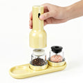 Yellow salt and pepper grinder set with a hand holding the top part on a white background