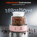 Pepper grinder with adjustable coarseness feature and pepper grains on a dark surface.